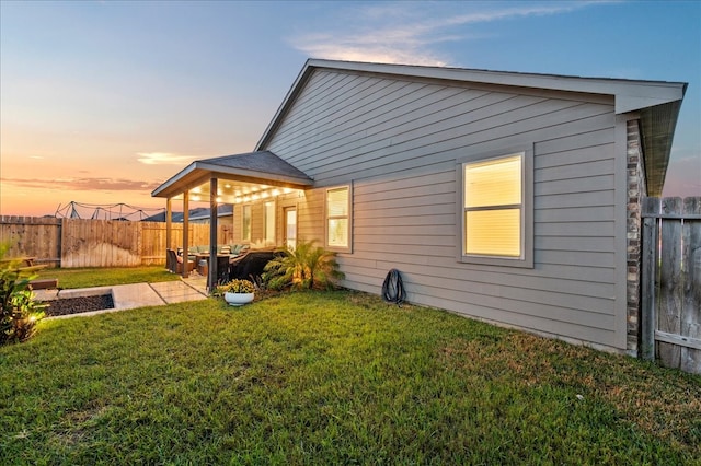 back house at dusk with a patio area and a lawn