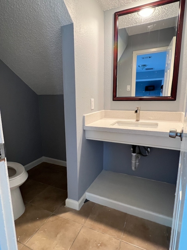 bathroom with toilet, a textured ceiling, sink, and tile patterned flooring