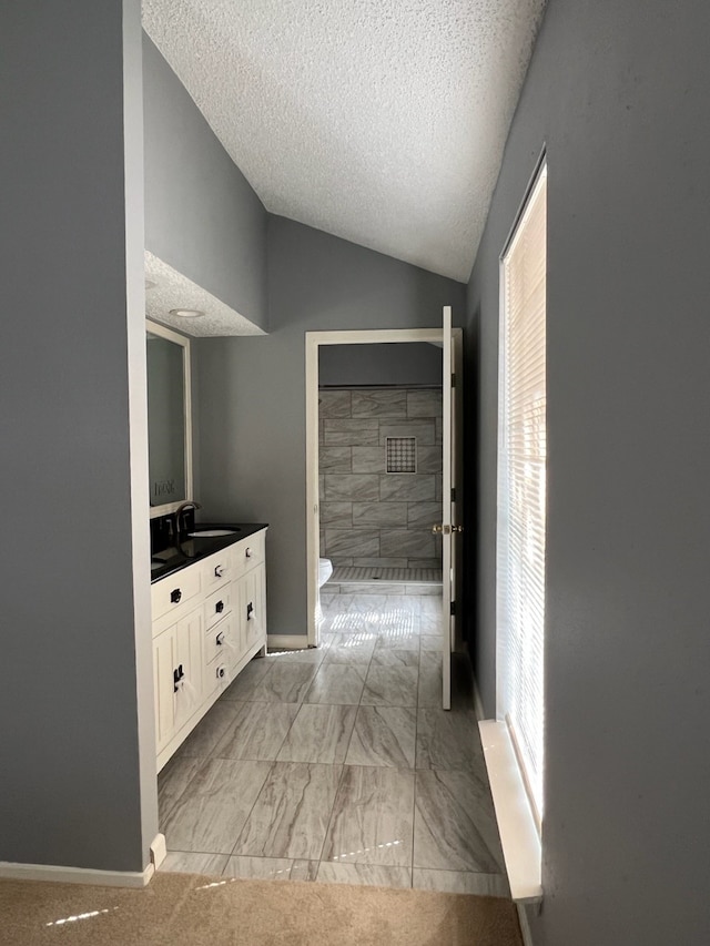 bathroom featuring lofted ceiling, a textured ceiling, toilet, plenty of natural light, and vanity