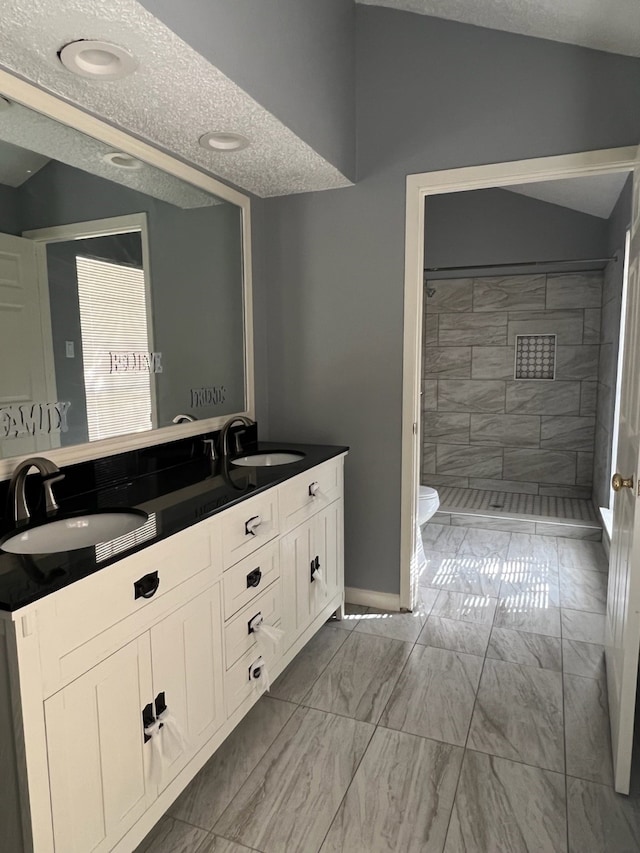 bathroom featuring a tile shower, a textured ceiling, toilet, lofted ceiling, and vanity