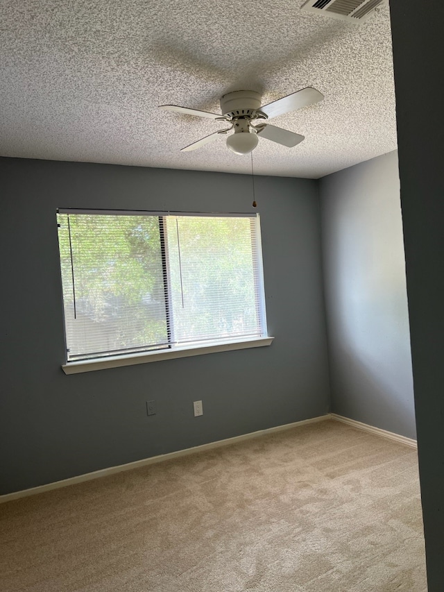 spare room with ceiling fan, a textured ceiling, and light colored carpet