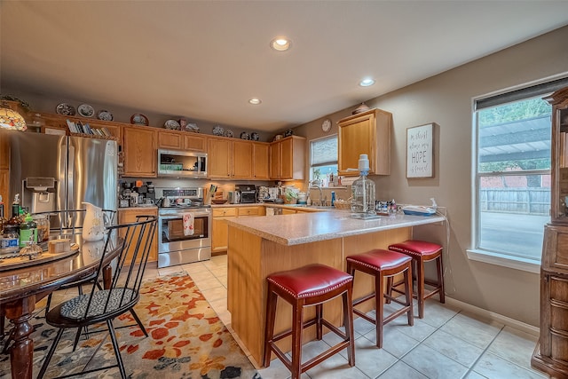 kitchen featuring kitchen peninsula, stainless steel appliances, sink, a kitchen bar, and light tile patterned floors