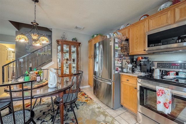 kitchen with light tile patterned flooring, a textured ceiling, hanging light fixtures, stainless steel appliances, and a chandelier