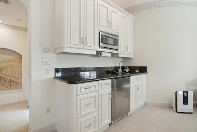 kitchen with white cabinets, light colored carpet, appliances with stainless steel finishes, and dark stone counters