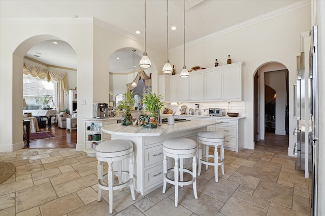 kitchen with a kitchen island with sink, crown molding, pendant lighting, white cabinets, and a breakfast bar area