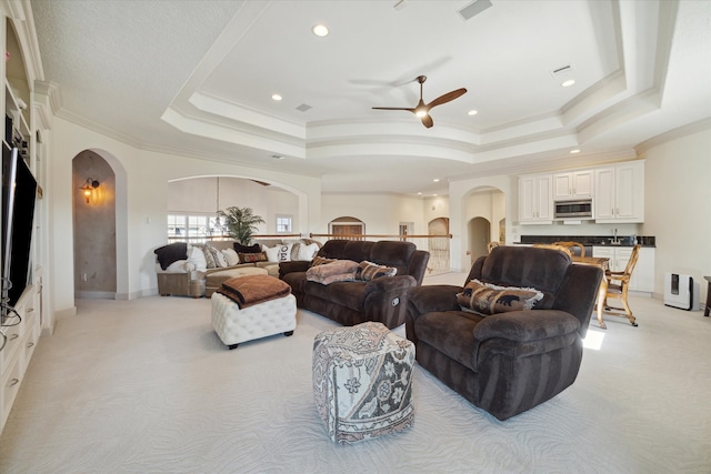 living room with a raised ceiling, light carpet, crown molding, and ceiling fan