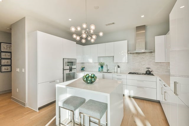 kitchen with a center island, wall chimney exhaust hood, sink, and white cabinets