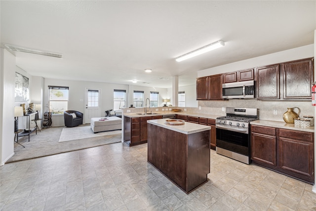 kitchen featuring sink, a center island, kitchen peninsula, dark brown cabinets, and appliances with stainless steel finishes