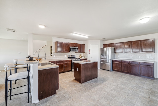 kitchen with a breakfast bar, sink, dark brown cabinetry, kitchen peninsula, and stainless steel appliances