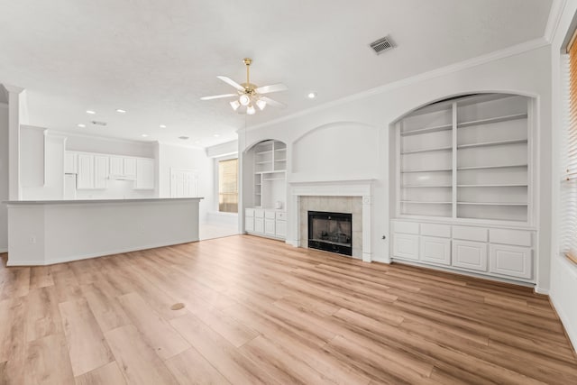 unfurnished living room featuring a tiled fireplace, ornamental molding, built in features, light hardwood / wood-style floors, and ceiling fan