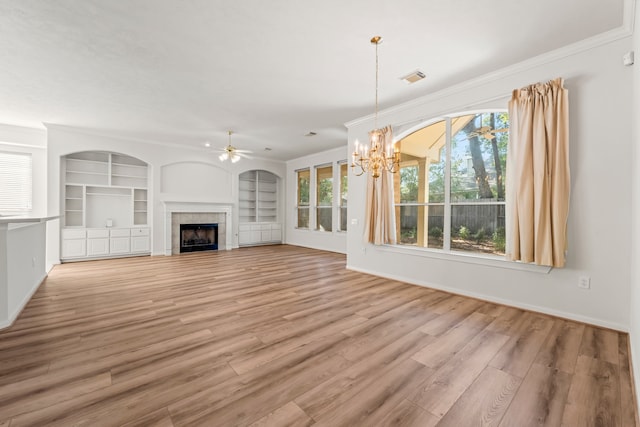 unfurnished living room with ceiling fan with notable chandelier, a tiled fireplace, ornamental molding, light hardwood / wood-style flooring, and built in shelves