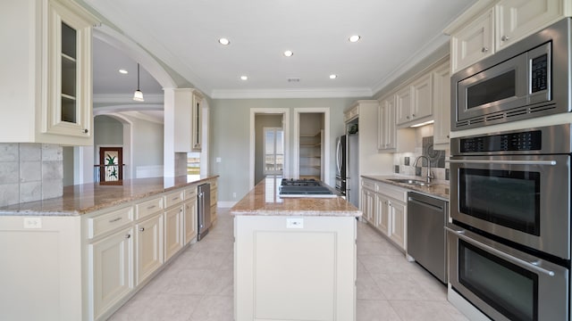 kitchen with light stone countertops, cream cabinets, kitchen peninsula, stainless steel appliances, and crown molding