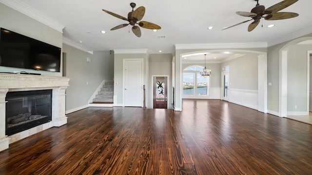 unfurnished living room featuring ceiling fan with notable chandelier, ornamental molding, dark wood-type flooring, and a fireplace