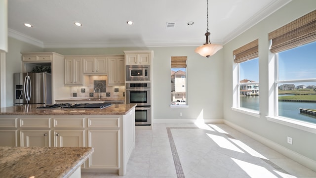 kitchen with cream cabinets, tasteful backsplash, light stone countertops, stainless steel appliances, and decorative light fixtures