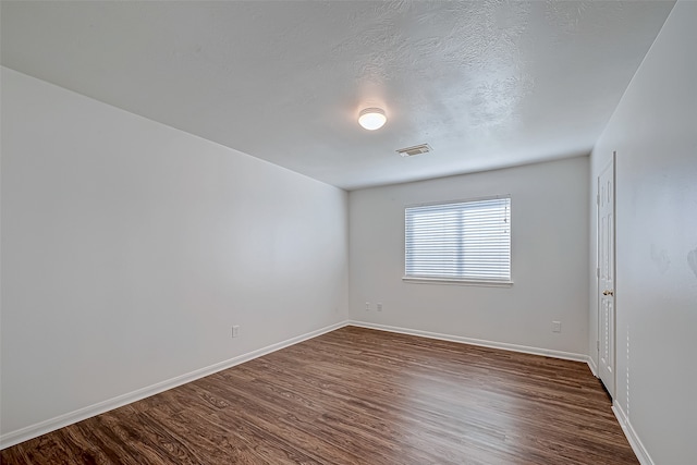 spare room featuring dark wood-type flooring and a textured ceiling