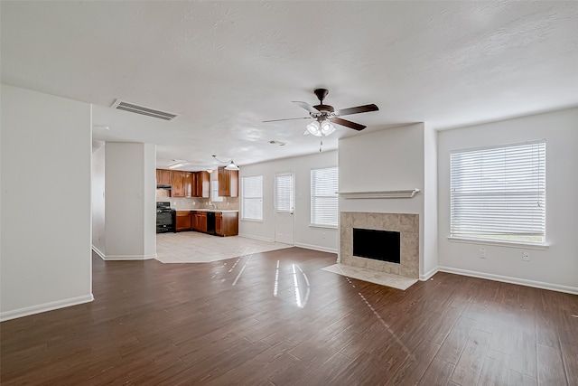 unfurnished living room with light wood-type flooring, ceiling fan, and a tiled fireplace