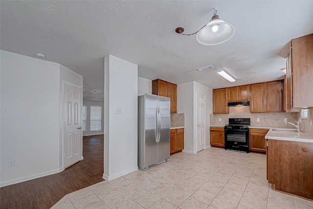 kitchen featuring stainless steel fridge, light wood-type flooring, tasteful backsplash, sink, and black gas range