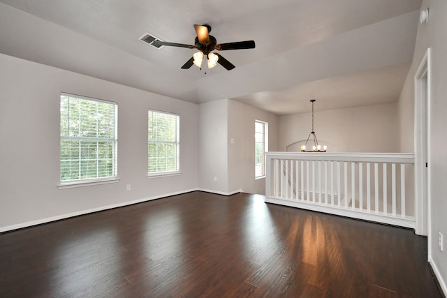 empty room with dark wood-type flooring, ceiling fan with notable chandelier, and plenty of natural light