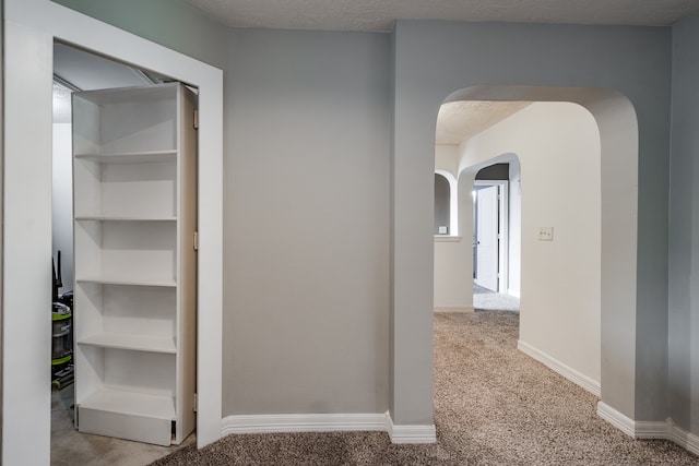 hallway featuring light colored carpet and a textured ceiling