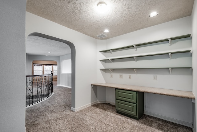 unfurnished office featuring built in desk, light colored carpet, and a textured ceiling