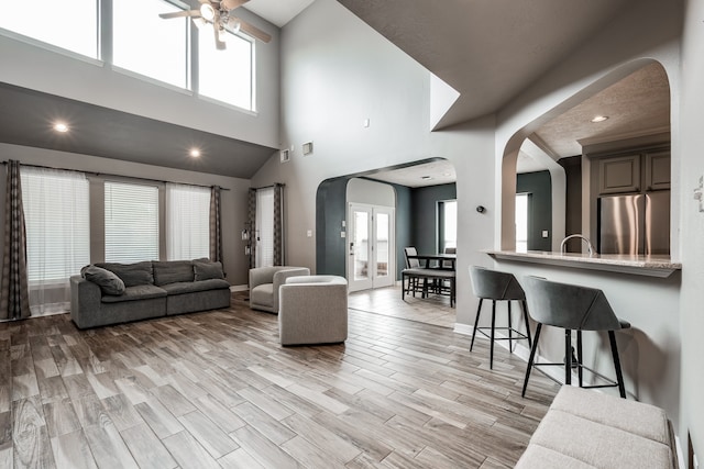 living room featuring a towering ceiling, light wood-type flooring, a textured ceiling, ceiling fan, and sink