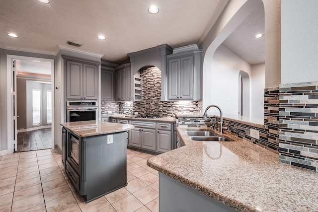 kitchen with light stone counters, gray cabinetry, stainless steel oven, crown molding, and sink