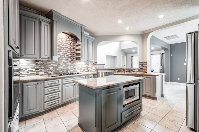 kitchen with tasteful backsplash, gray cabinetry, a kitchen island, and appliances with stainless steel finishes