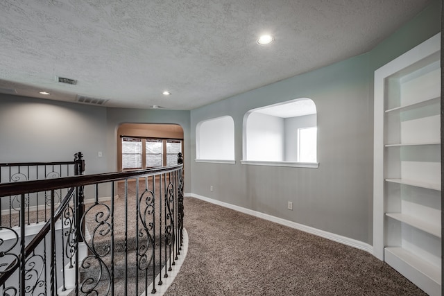 hall with built in shelves, carpet floors, and a textured ceiling