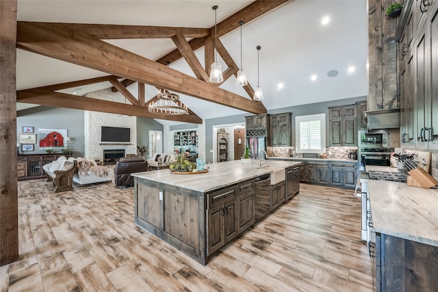 kitchen featuring a stone fireplace, pendant lighting, high vaulted ceiling, light stone countertops, and a spacious island