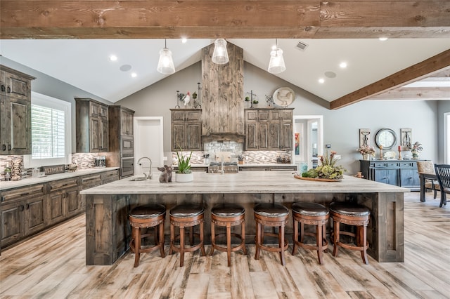 kitchen with backsplash, a large island with sink, and light wood-type flooring