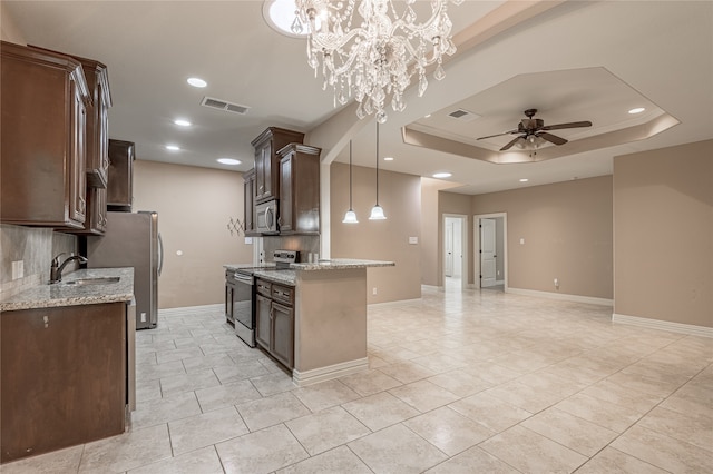 kitchen featuring stainless steel appliances, decorative light fixtures, a raised ceiling, light stone countertops, and sink