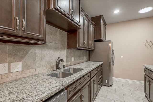 kitchen featuring light stone counters, stainless steel appliances, dark brown cabinetry, decorative backsplash, and sink