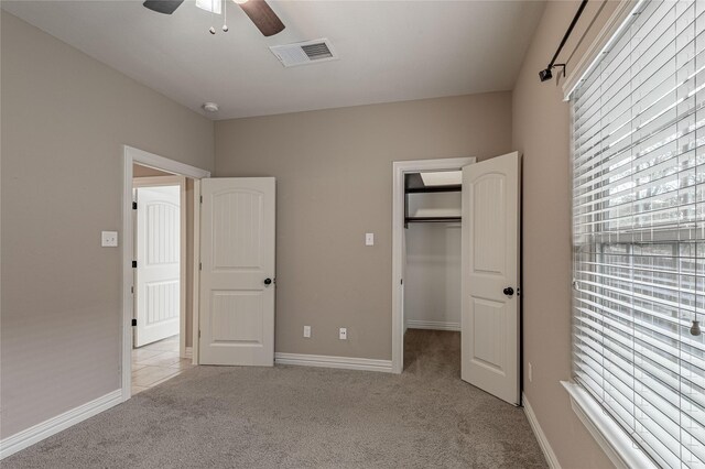 unfurnished bedroom featuring ceiling fan, a closet, a walk in closet, and light colored carpet