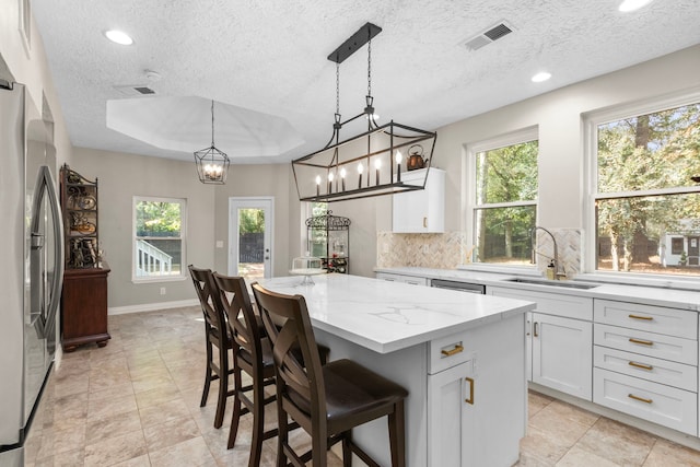 kitchen featuring sink, a kitchen island, a textured ceiling, hanging light fixtures, and white cabinetry