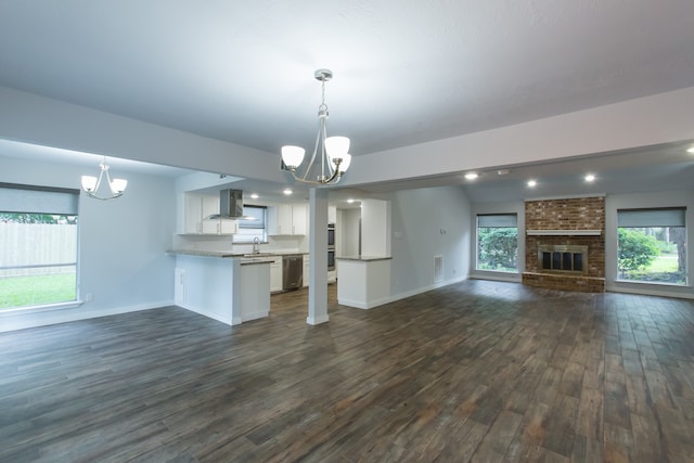 unfurnished living room featuring dark wood-type flooring, a notable chandelier, a fireplace, and a healthy amount of sunlight