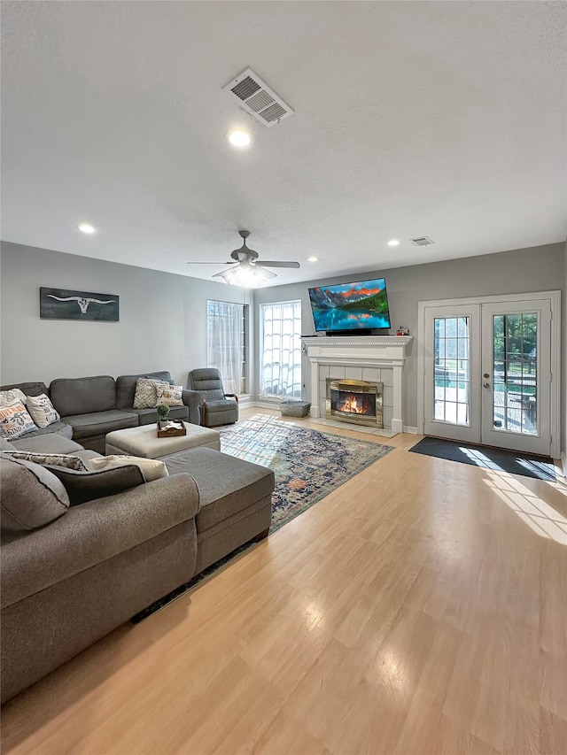 living room featuring a tile fireplace, french doors, light wood-type flooring, and ceiling fan