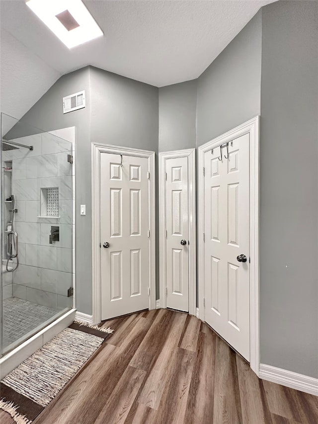 bathroom featuring hardwood / wood-style floors, walk in shower, and vaulted ceiling