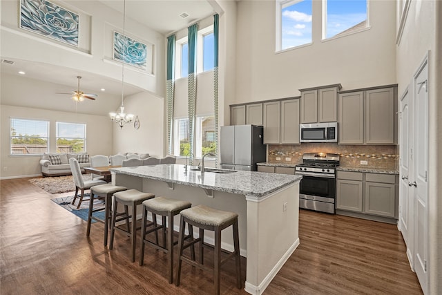 kitchen with light stone counters, appliances with stainless steel finishes, a towering ceiling, dark wood-type flooring, and gray cabinetry