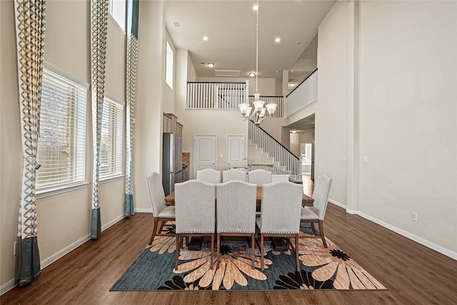 dining space featuring a towering ceiling, dark wood-type flooring, and a chandelier