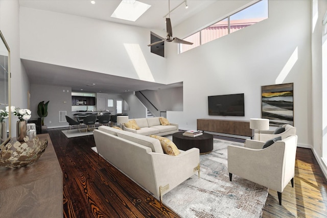 living room featuring ceiling fan, track lighting, dark wood-type flooring, and a high ceiling