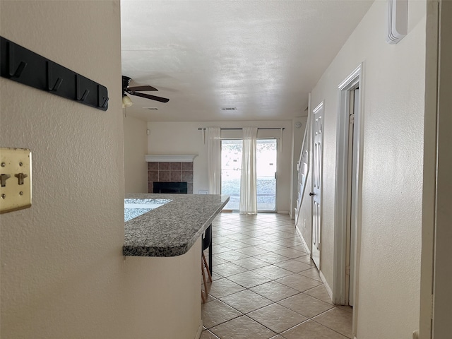 kitchen featuring kitchen peninsula, ceiling fan, a kitchen bar, light tile patterned flooring, and a fireplace