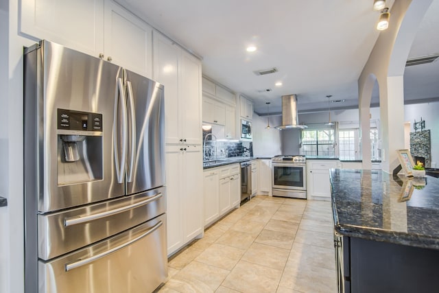 kitchen featuring white cabinets, dark stone countertops, appliances with stainless steel finishes, island range hood, and kitchen peninsula