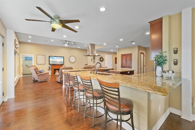 kitchen featuring a breakfast bar area, kitchen peninsula, light stone counters, and dark hardwood / wood-style flooring