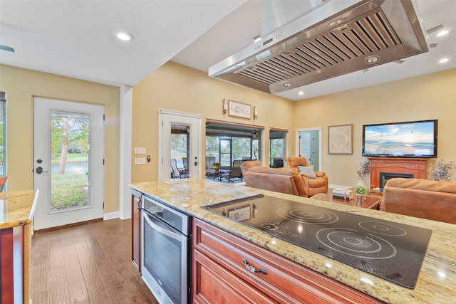 kitchen featuring light stone counters, black electric cooktop, dark wood-type flooring, wall chimney range hood, and oven