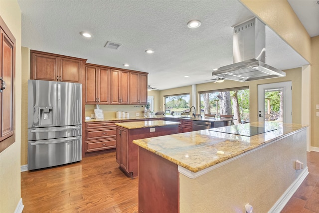 kitchen featuring hardwood / wood-style floors, island range hood, a kitchen island, kitchen peninsula, and stainless steel appliances