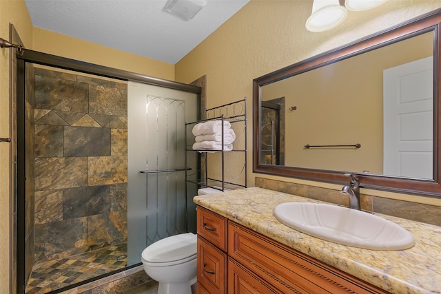 bathroom with a textured ceiling, vanity, toilet, and a shower with door