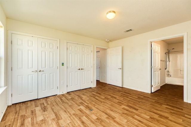 unfurnished bedroom featuring ensuite bathroom, wood-type flooring, and multiple closets