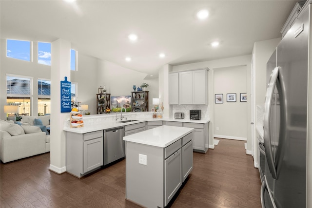 kitchen featuring kitchen peninsula, appliances with stainless steel finishes, sink, a center island, and dark hardwood / wood-style floors