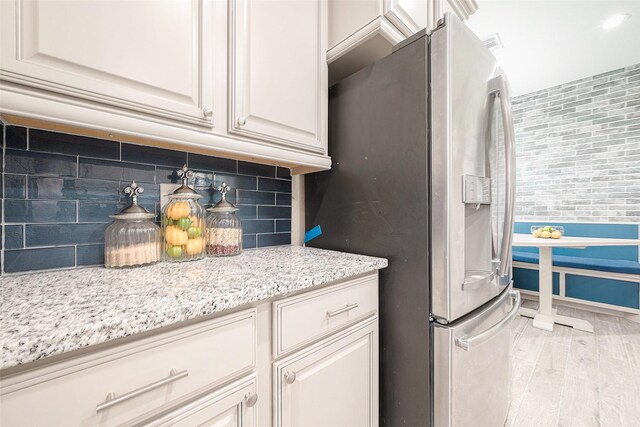 kitchen featuring white cabinets, stainless steel fridge, tasteful backsplash, light hardwood / wood-style floors, and light stone counters