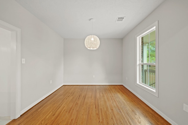 empty room featuring an inviting chandelier, light hardwood / wood-style flooring, and a wealth of natural light